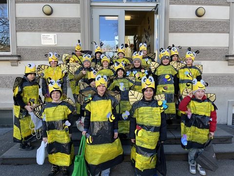 Kinder der Klassen 4a und 4b als Bienen verkleidet als Gruppe vor dem Schulgebäude