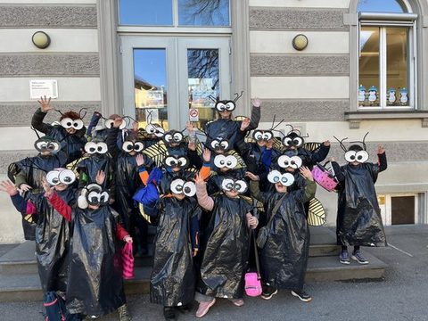 Kinder der Klassen 2a und 2b als Fliegen verkleidet als Gruppe vor dem Schulgebäude